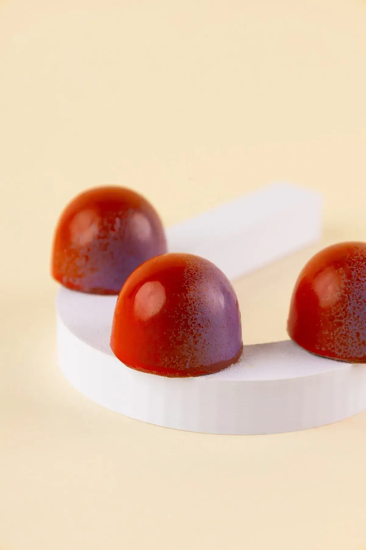 Três bombons vermelhos com degradê roxo sobre bases brancas